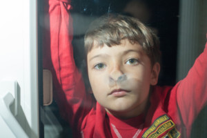 Little boy looking through window glass indoors