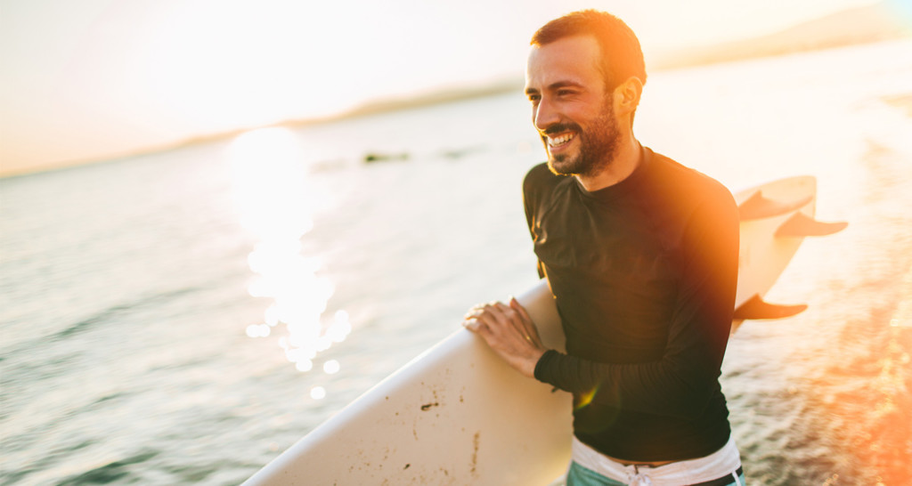 Man smiling in sunlight with surfboard 