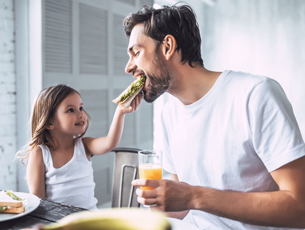 Man being fed sandwich by young child