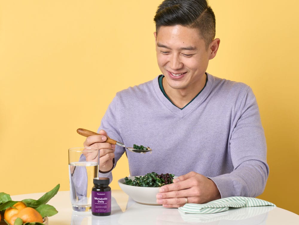 Man eating a salad with a bottle of Pendulum GLP-1 daily supplement for metabolism next to him