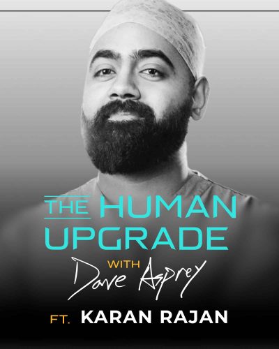 A bearded man in medical scrubs poses confidently. Text reads: The Human Upgrade with Dave Asprey ft. Karan Rajan on a gray gradient background.