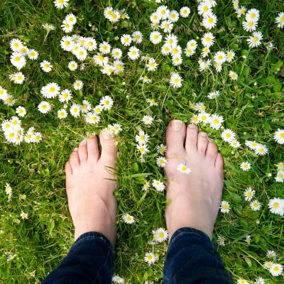 Female,Feet,Standing,On,Green,Grass,And,White,Flowers,-