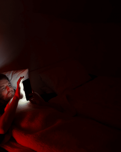 Man laying in bed reading from a smartphone