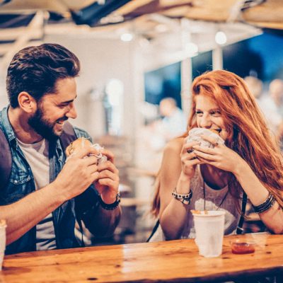 A young couple having snack and drink at an outdoors music festival. Eating burgers with fries and drinking beer.